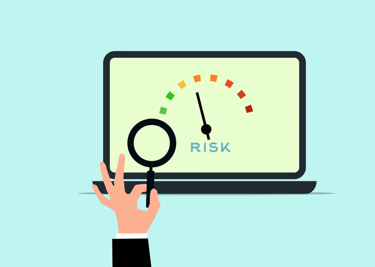 A computer screen shows a dial from green (low risk) to red (high risk) and a hand holding a magnifying glass.